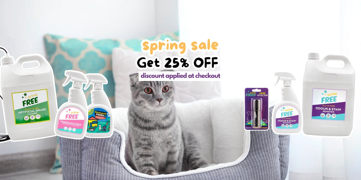 A gray tabby cat sits in a white pet bed in a bright room, surrounded by floating bottles and sprayers of urineFREE products with a 'Spring sale Get 25% OFF' promotional text overlay.
